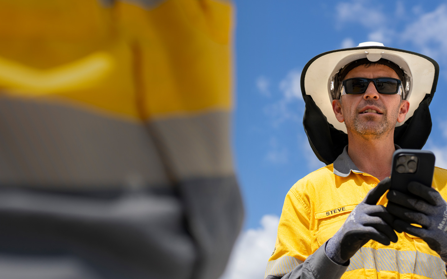 Un trabajador sobre el terreno vestido con un equipo de seguridad sostiene un iPhone mientras habla con un miembro del equipo