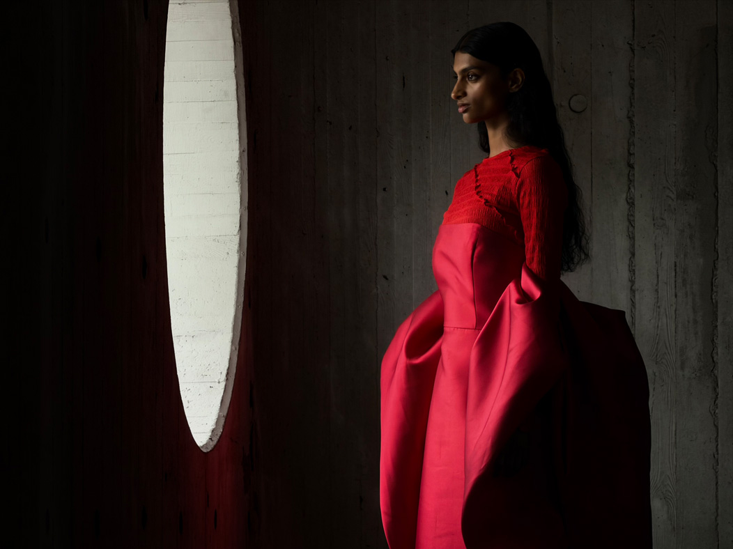 A woman wearing a long red dress stands in an empty room being photographed. The Photo app toggles through the focal lengths to demonstrate the capabilities of the pro camera system, showcasing: 200 mms